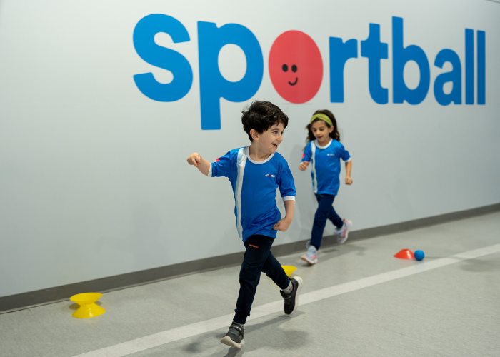 Children running during Sportball kids sports program, with colorful equipment on floor.