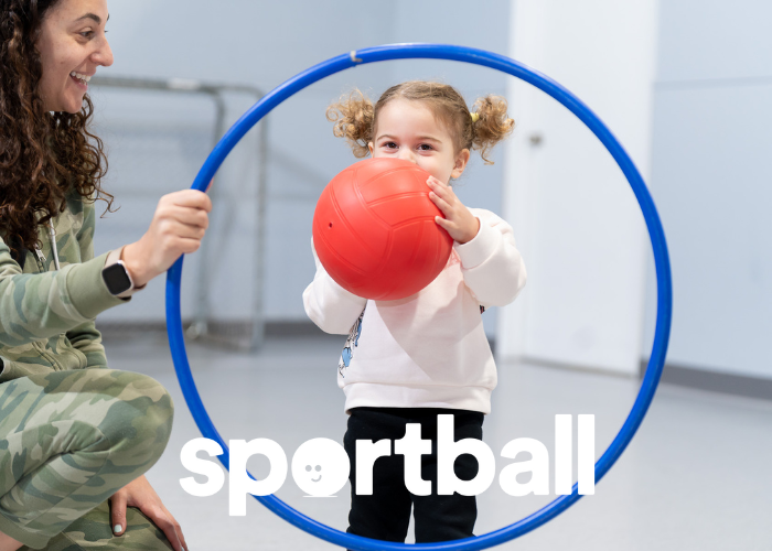 Young girl holding red ball, framed by blue hoop in Sportball kids sports program.