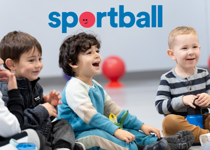 Three smiling boys participating in Sportball kids sports program, sitting on floor.