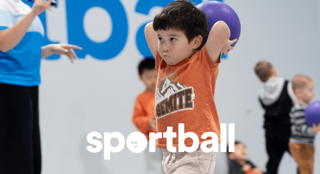 Young boy holding purple ball overhead during kids sports program.