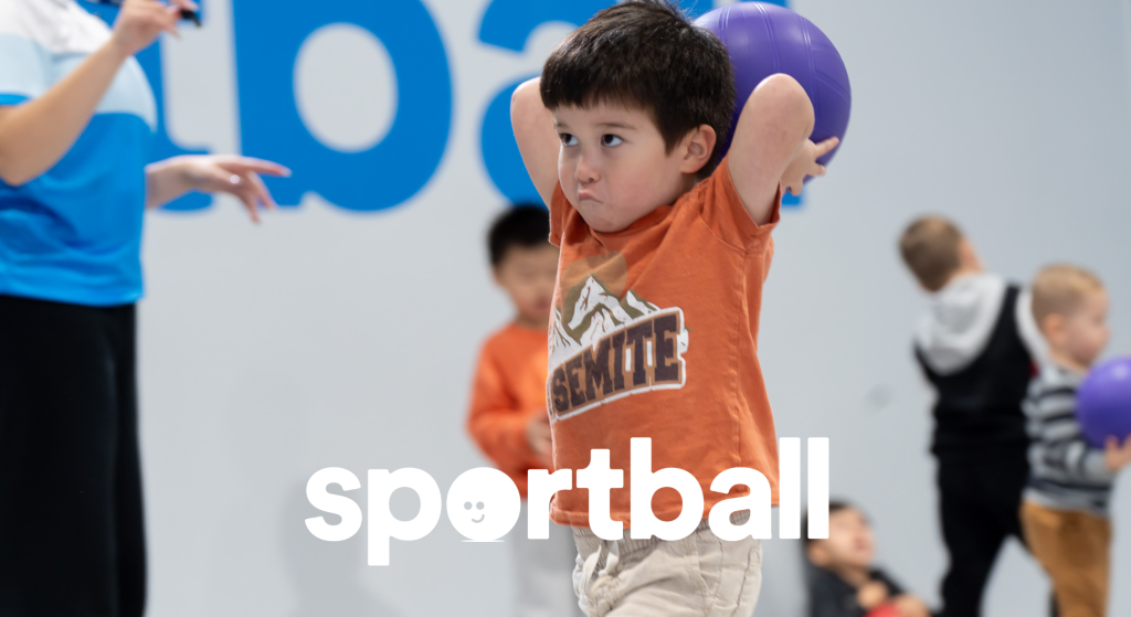 Young boy holding purple ball overhead during kids sports program.