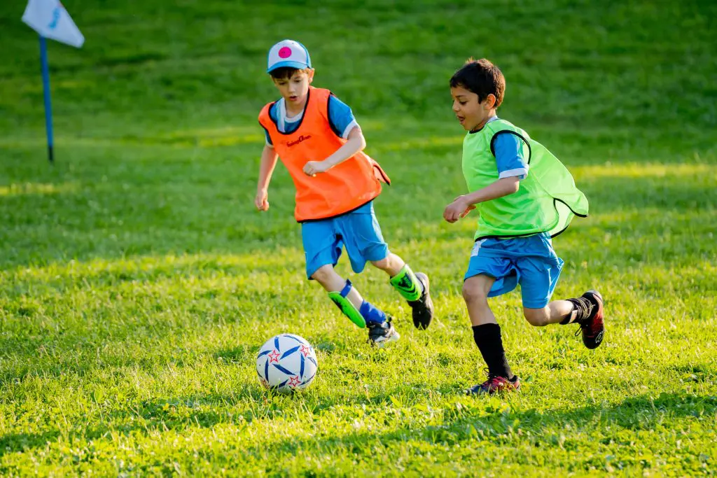 Two children playing soccer in different coloured bibs.